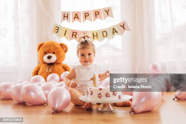 the adorable baby girl is sitting on the floor and eating  her delicious first birthday cake. cake smash. - smash cake stockfoto's en -beelden