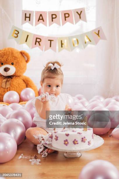 cake smash. birthday girl is trying her first birthday cake while sitting on the floor. - smash cake bildbanksfoton och bilder