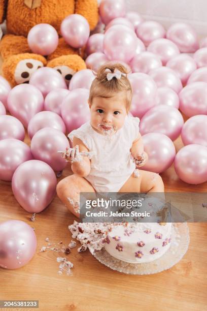 cake smash. birthday girl is trying her first birthday cake while sitting on the floor. - smash cake stockfoto's en -beelden