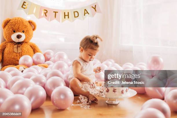 cake smash. birthday girl is trying her first birthday cake while sitting on the floor. - smash cake stockfoto's en -beelden