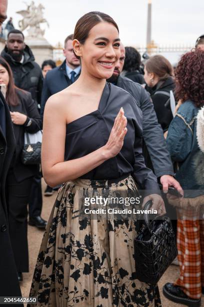 Kimberley Anne Woltemas wears black one sleeve shirt, beige and black printed pleated maxi skirt, black Dior bag, outside Dior, during the Womenswear...