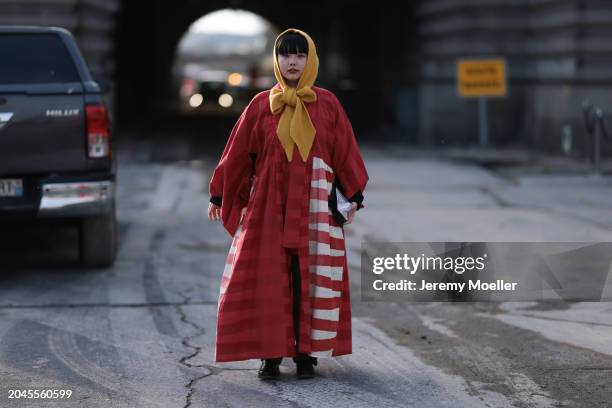 Guest wears a yellow head scarf / piece with a bow detail, red / white striped oversized kimono inspired long coat, khaki long suit pants and black...