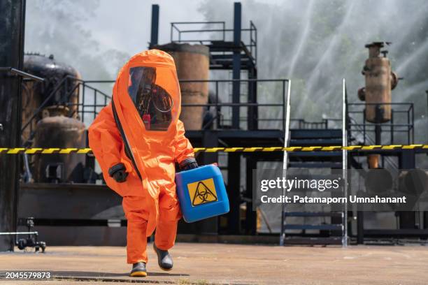 exterminador de productos químicos dedicado, vestido con un traje de materiales peligrosos, que lleva cuidadosamente un galón de productos químicos fuera de una fábrica. esencia de peligrosidad y precisión que intervienen en los procesos de exterminio - señal de advertencia radioactiva fotografías e imágenes de stock
