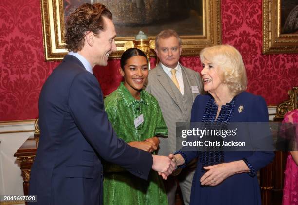 Queen Camilla shakes hands with Tom Hiddleston during a reception for the BBC's 500 Words Finalists at Buckingham Palace on February 28, 2024 in...