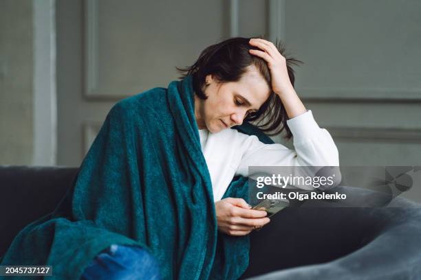 staying home due to menstruation: sad woman in a blanket, stays home with her smartphone - sick stock pictures, royalty-free photos & images