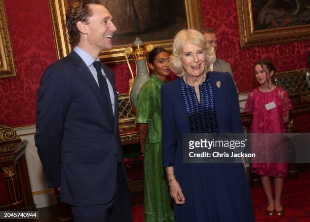 Queen Camilla shares a joke with Tom Hiddleston during a reception for the BBC's 500 Words Finalists at Buckingham Palace on February 28, 2024 in...