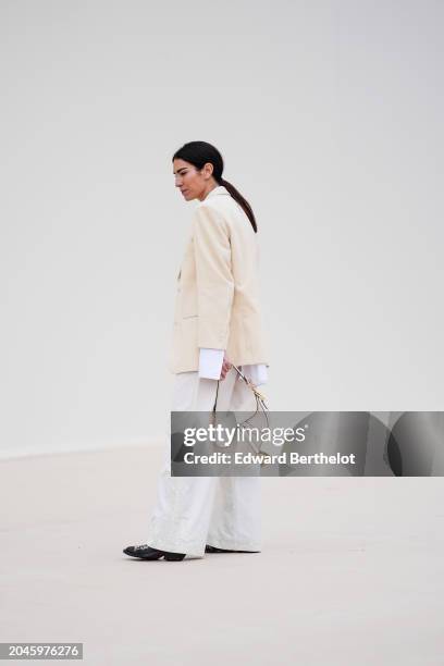 Guest wears a white oversized blazer jacket, a white shirt, flared pants , black shoes, a Dior Saddle bag outside Dior, during the Womenswear...