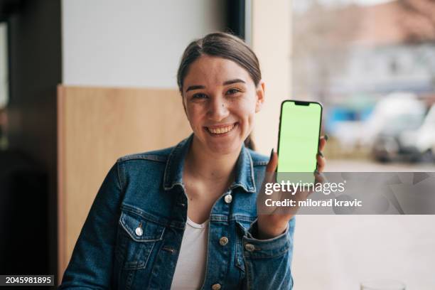 mujer joven con teléfono de pantalla verde - exhibir fotografías e imágenes de stock