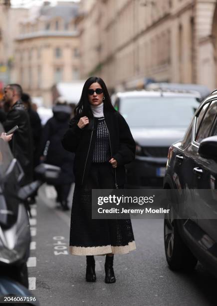 Guest seen wearing black sunglasses, silver earrings, white cotton turtleneck top, black / beige crochet pleated long dress, black oversized bomber...