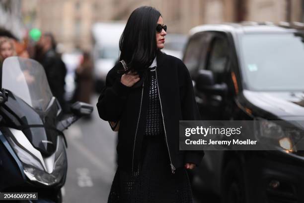 Guest seen wearing black sunglasses, silver earrings, white cotton turtleneck top, black / beige crochet pleated long dress, black oversized bomber...