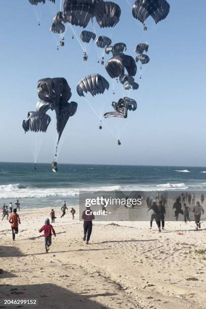 This image grab from an AFPTV video shows Palestinians running toward parachutes attached to food parcels, airdropped from US aircrafts on a beach in...