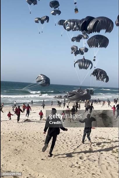 This image grab from an AFPTV video shows Palestinians running toward parachutes attached to food parcels, airdropped from US aircrafts on a beach in...