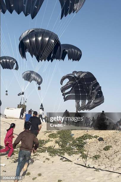 This image grab from an AFPTV video shows Palestinians running toward parachutes attached to food parcels, airdropped from US aircrafts on a beach in...