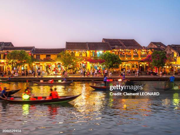 riverbank of hoi an at night with vietnamese traditional houses and wooden rowing boats decorated with paper lanterns on the river, old town of hoi an - unesco world heritage site - quang nam province - central vietnam. - hoi an stock pictures, royalty-free photos & images
