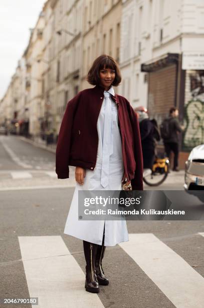 Flora Coquerel wears white or pale blue dress, tie, burgundy jacket, black boots and a burgundy bag outside Casablanca during the Womenswear...