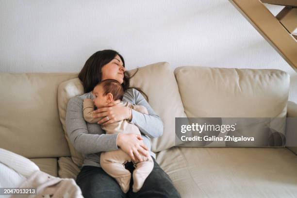 tired young woman mother fell asleep while holding baby on her hands on the couch at home - postpartum depression stock pictures, royalty-free photos & images