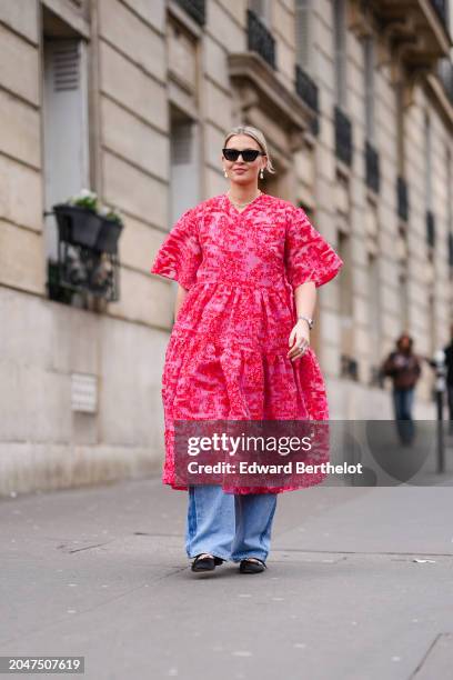 Guest wears sunglasses, a pink floral print oversized gathered / pleated midi dress , a JW Anderson leather bag, blue wide-leg flared denim pants /...