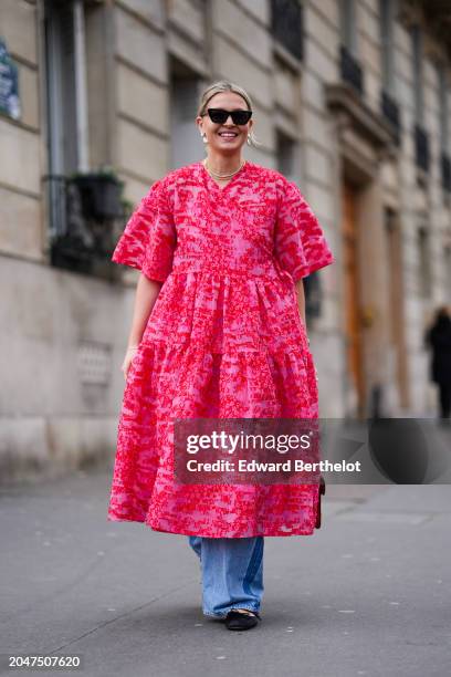 Guest wears sunglasses, a pink floral print oversized gathered / pleated midi dress , a JW Anderson leather bag, blue wide-leg flared denim pants /...
