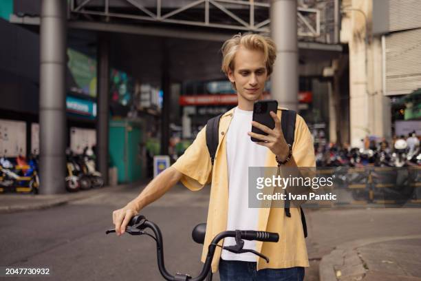 carefree man with a bike using mobile phone in the city. - city life authentic stock pictures, royalty-free photos & images