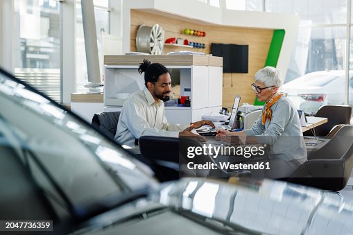 Smiling salesperson explaining contract to customer at desk Smiling salesperson explaining contract to customer at desk