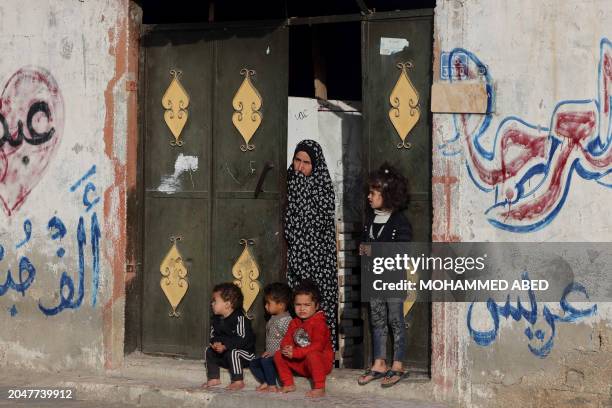 Palestinian woman stands next to children at the gate of their home during the funeral of twin babies killed in an overnight Israeli air strike, in...