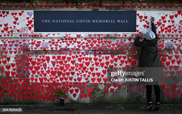 Person writes on The National Covid Memorial Wall, dedicated to those who lost their lives to Covid-19, on the embankment on the south side of the...