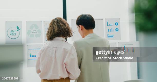 two asian professionals stand in a board room, discussing strategies for environmental conservation and sustainable business development. esg sustainable business office. - maatschappelijk verantwoord ondernemen stockfoto's en -beelden