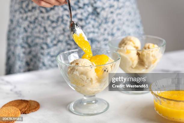 woman putting fruit sauce on ice cream in bowl - sundae stockfoto's en -beelden