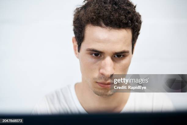 beau jeune homme regardant sérieusement alors qu’il travaille à un ordinateur - regarder vers le bas photos et images de collection
