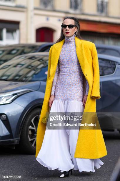 Guest wears sunglasses, red lipstick, a yellow fluffy long wool coat , a floral print turtleneck top / long dress with gathered bottom part, outside...