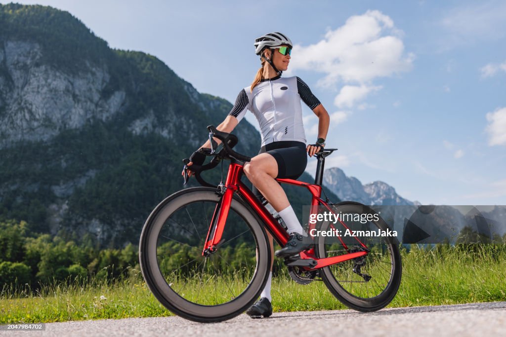 Professional Female Cyclist Looking Around While Standing On A Country Road With A Bicycle Between Her Legs