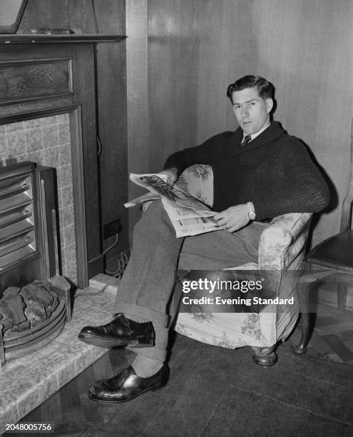 Tottenham Hotspur Football Club goalkeeper Ron Reynolds seated in front of a fireplace with a newspaper, March 8th 1956.