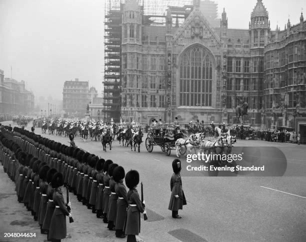 Footguards of the Household Division line the route opposite the Houses of Parliament as a royal carriage approaches during the State Opening of...