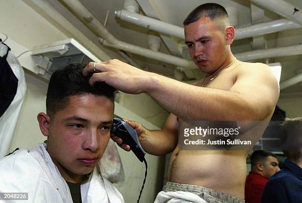 Navy Petty Officer Willie Cinco of Houston, Texas cuts the hair of USMC Lance Corpral Conrad Munoz of Buena Park, California on the USS Constellation...