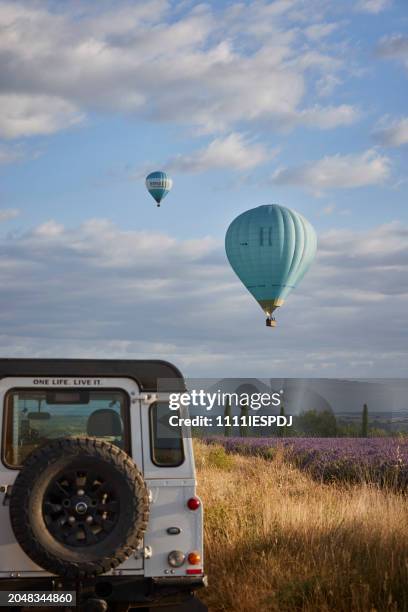 land rover 4x4 auf der straße neben einem lavendelfeld in der provence, frankreich (plateau de valensole), zwei heißluftballons schweben in der luft - ballon de basket stock-fotos und bilder