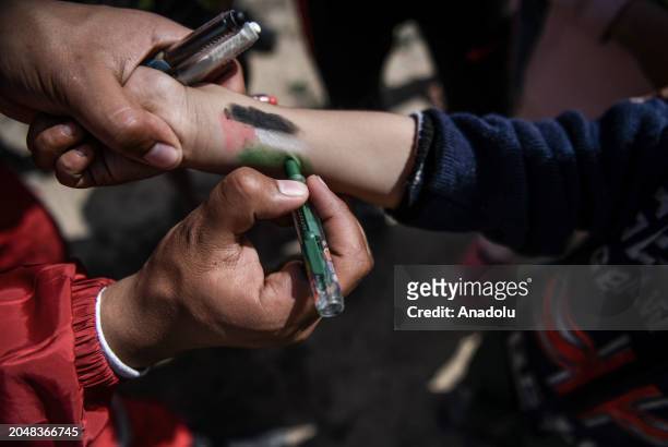 An official draws Palestinian flag on child's wrist as Officials from Egyptian Red Crescent and the Palestinian Red Crescent organize an event...