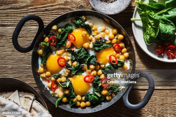 chickpea and spinach shakshuka in cooking pan, sunlight with harsh shadows - cucina del medio oriente foto e immagini stock