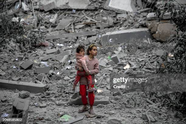 Palestinian girl carries a child through the rubble of houses destroyed by Israeli bombardment in Gaza City on March 3 amid the ongoing conflict...