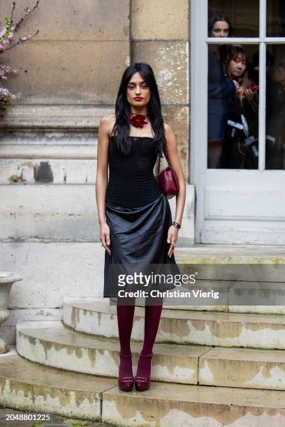 Sabrina Bahsoon wears burgundy Roger Vivier bag, heels, tights, black leather skirt, off shoulder top outside of "VIVIER OP-TICAL" - Roger Vivier...