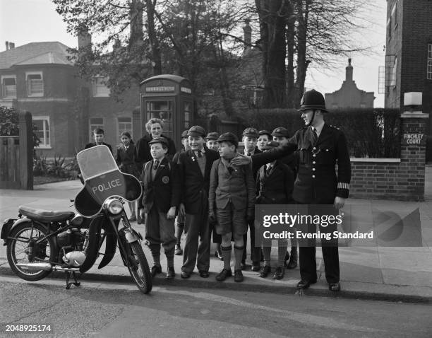 Police Constable R Baldwin stands with a group of children on the edge of a pavement beside his parked motorbike during a road safety exercise...