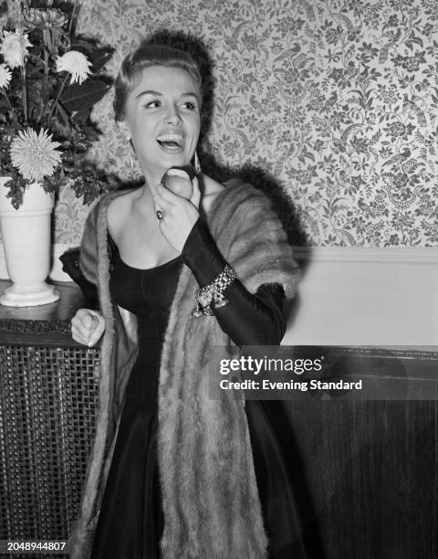 British singer Yana laughs while holding a bitten apple, December 9th 1955.