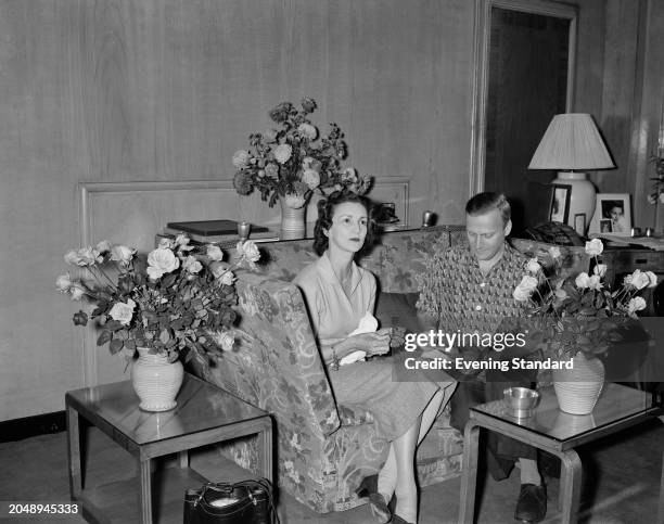 Diana Gould with her husband, violinist Yehudi Menuhin seated on a sofa between vases of roses, November 26th 1955.