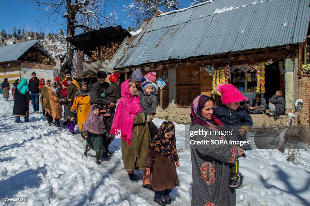 Parents carrying their children queue along a snow-covered...