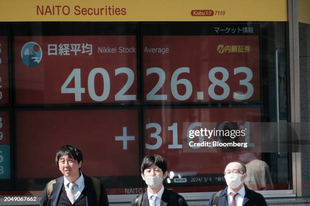 Pedestrians in front of an electronic stock board showing the Nikkei 225 Stock Average outside a securities firm in Tokyo, Japan, on Monday, March 4,...