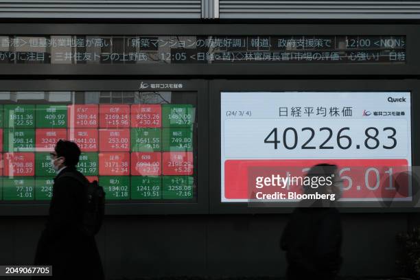 Pedestrians in front of an electronic stock board showing the Nikkei 225 Stock Average outside a securities firm in Tokyo, Japan, on Monday, March 4,...