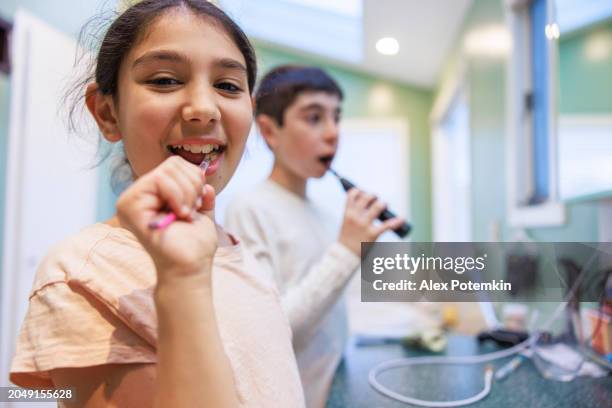 happy kids posing for the camera while brushing teeth in a bathroom - fluor stockfoto's en -beelden