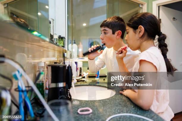 young boy and girl brushing their teeth together in the bathroom - fluor stockfoto's en -beelden