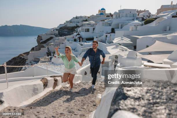 excited young tourist couple running and holding hands while exploring the greek villages - village couple stock pictures, royalty-free photos & images
