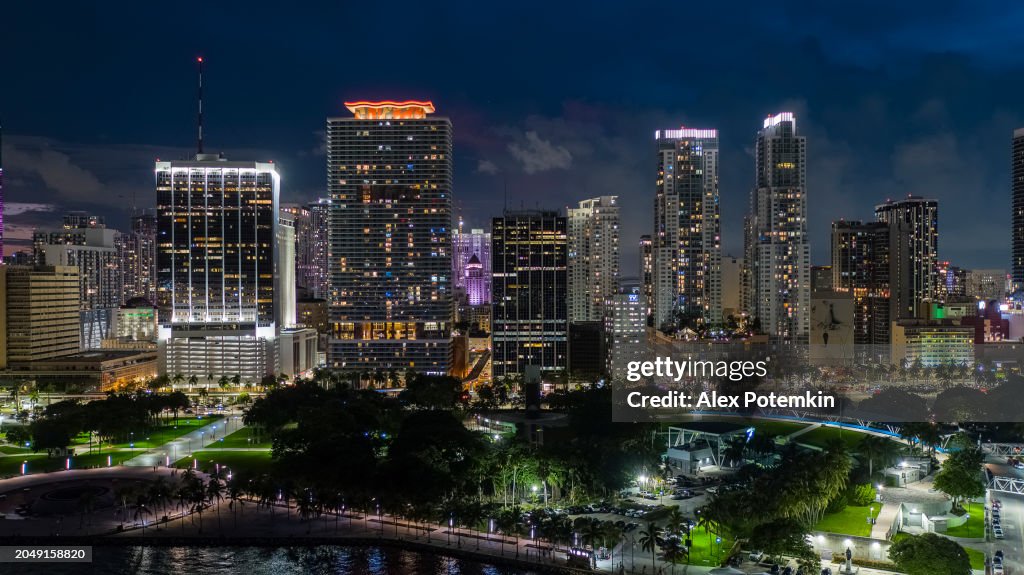 Neon office buildings stands behind the Bayfront Park in Downtown Miami, FL. Illuminated Downtown skyscrapers cityscape in twilight.