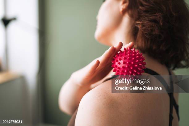 brunette smiling young woman in sports uniform doing self-massage with massage ball after fitness exercises at home - massage ball stock pictures, royalty-free photos & images